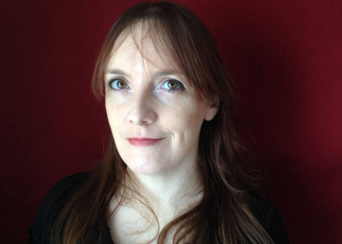 Headshot of Lisa McInerney. The author has long brown hair with a fringe. She stands in front of a red wall and smiles at the viewer.