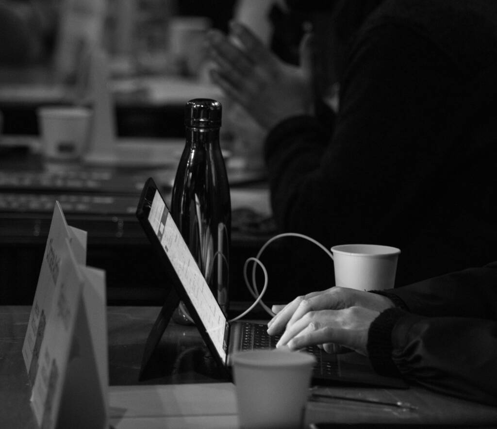 Hands type on a laptop beside two cups and a water bottle