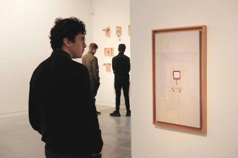 A person stops to look at an artwork in a white gallery space.