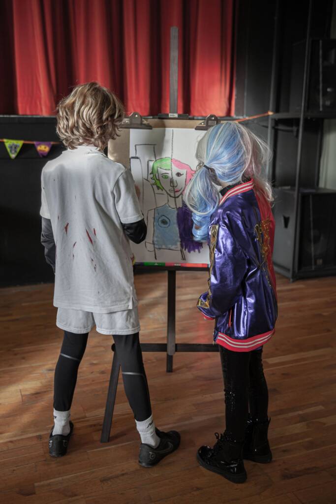 two young artists paint two sides of a person split down the middle.